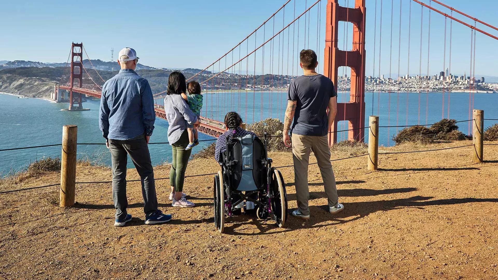 一群人, 包括一个坐轮椅的人, 从后面看, während sie von den Marin Headlands aus auf die 金门大桥 blicken.