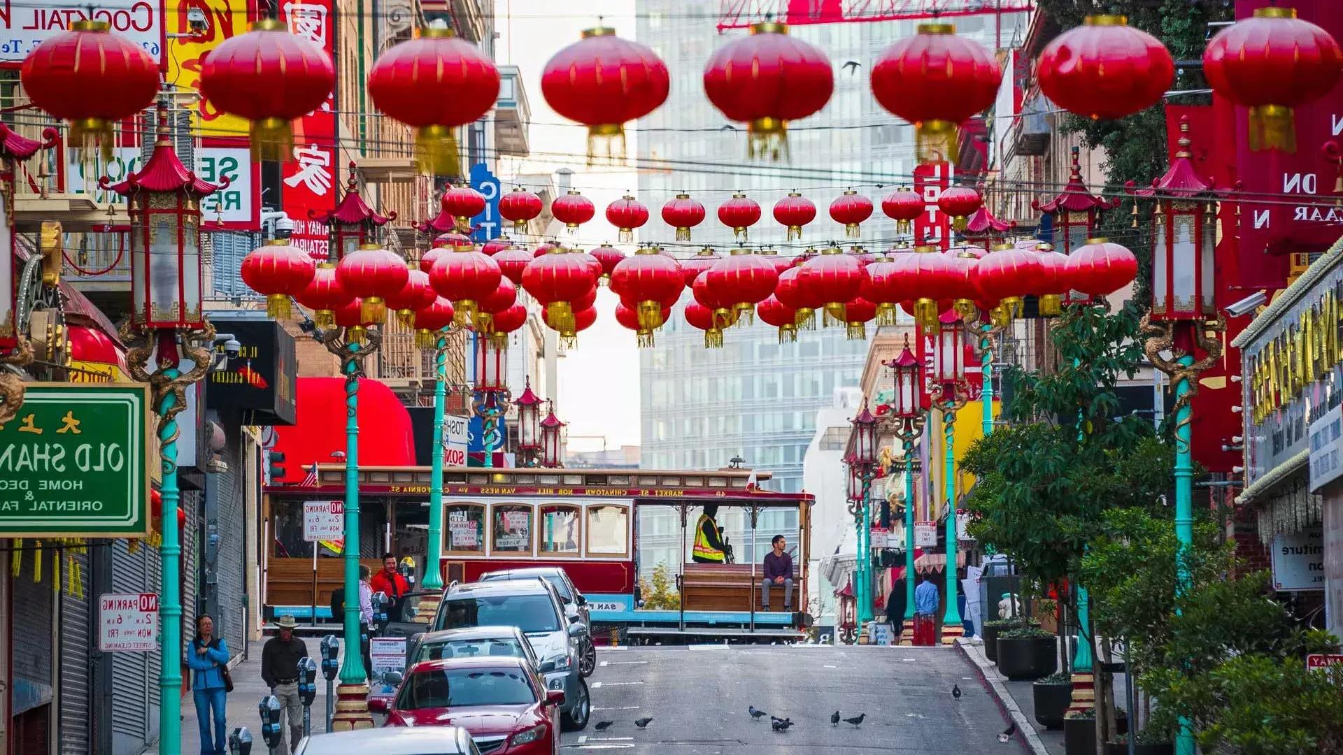 A hilly street in San Francisco's 唐人街 is pictured with red lanterns dangling and a streetcar passing by.