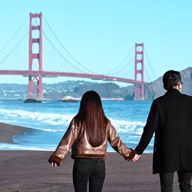 以金门大桥为背景的贝克海滩情侣手牵着手 